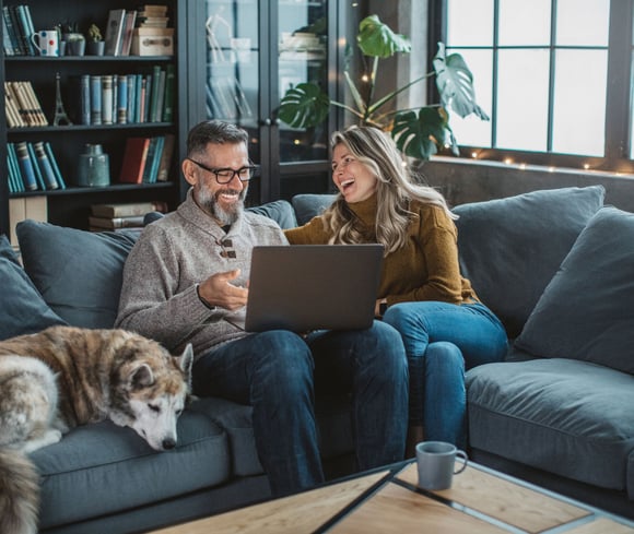 Mature couple sitting on the couch with their dog and looking at laptop image